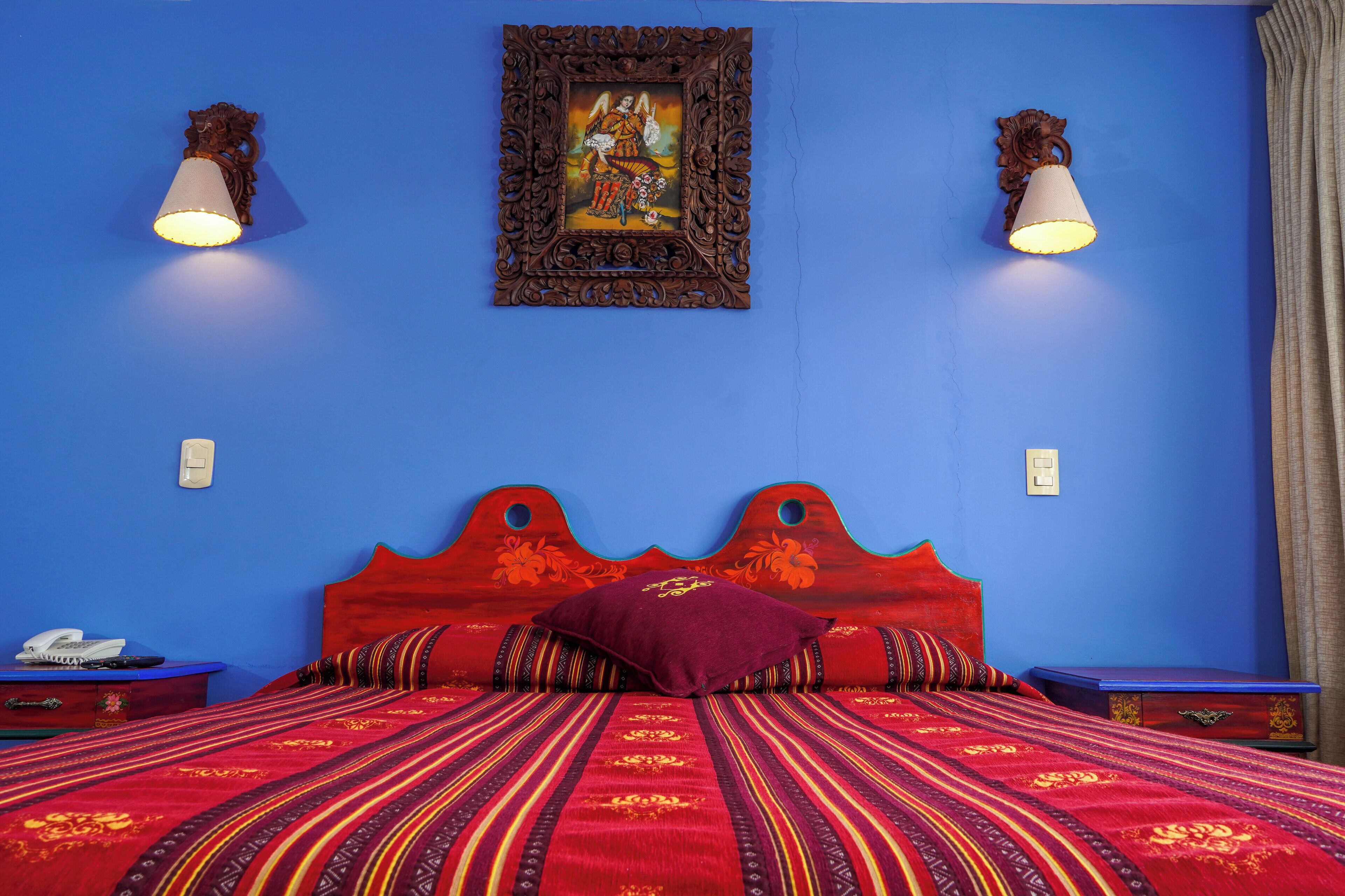 A room with a wooden headboard, a patterned bedspread, and two wall-mounted lamps.