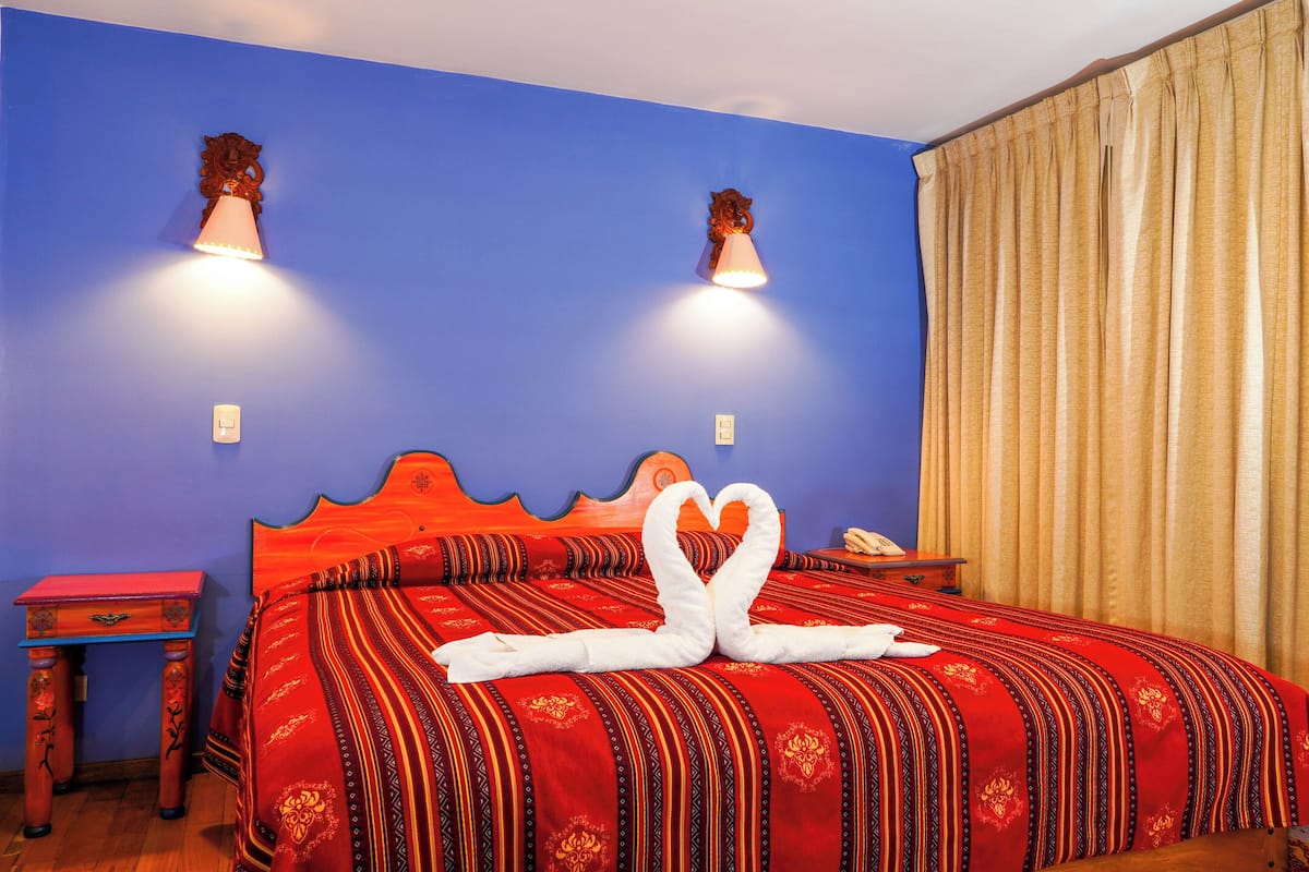 Habitación de hotel con una cama grande, cabecera de madera, dos mesitas de noche y una cortina.