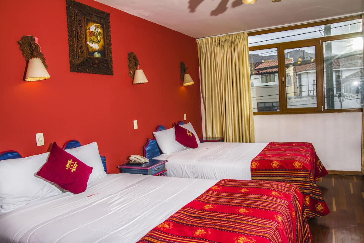 Habitación de hotel con dos camas, paredes rojas y ventana con vistas a edificios.