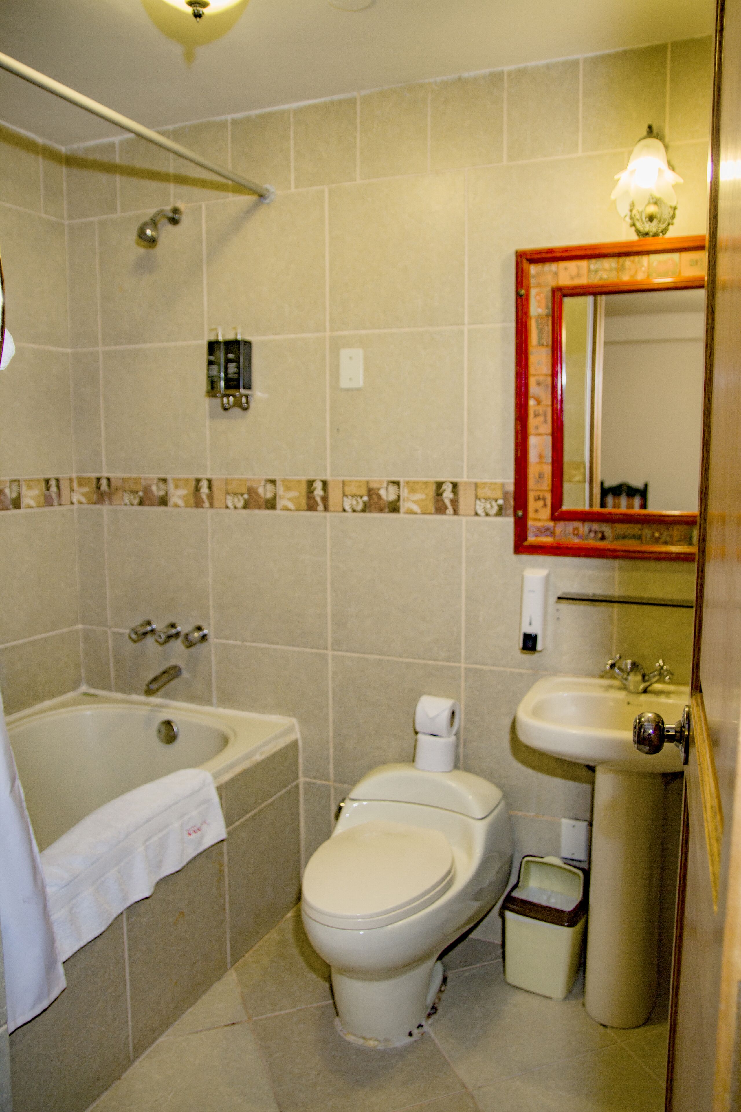 A standard bathroom with a bathtub, toilet, sink, and a mirror with a decorative frame.