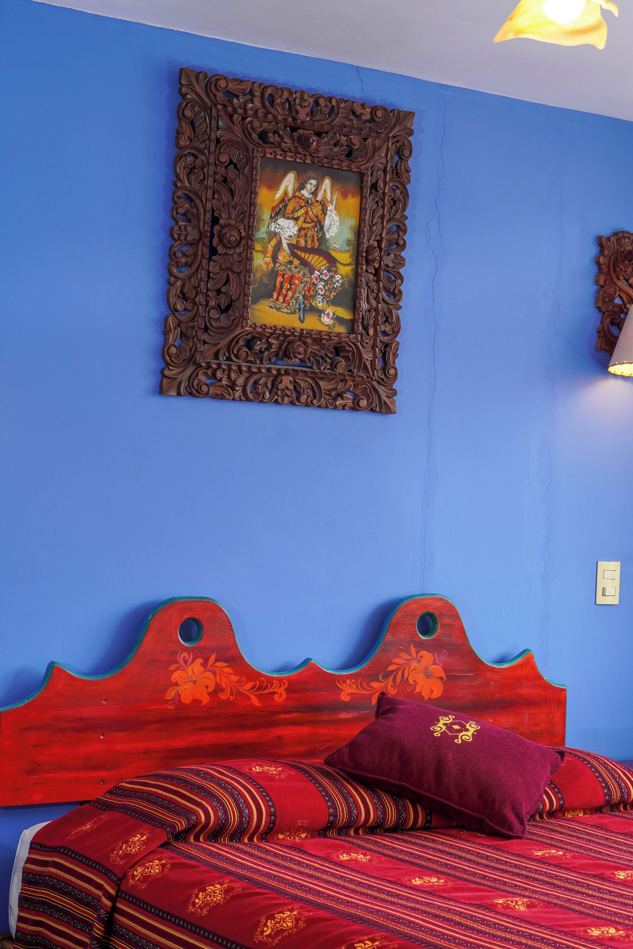 A room with a blue wall, a wooden bed frame with a floral design, and a framed picture above the bed.