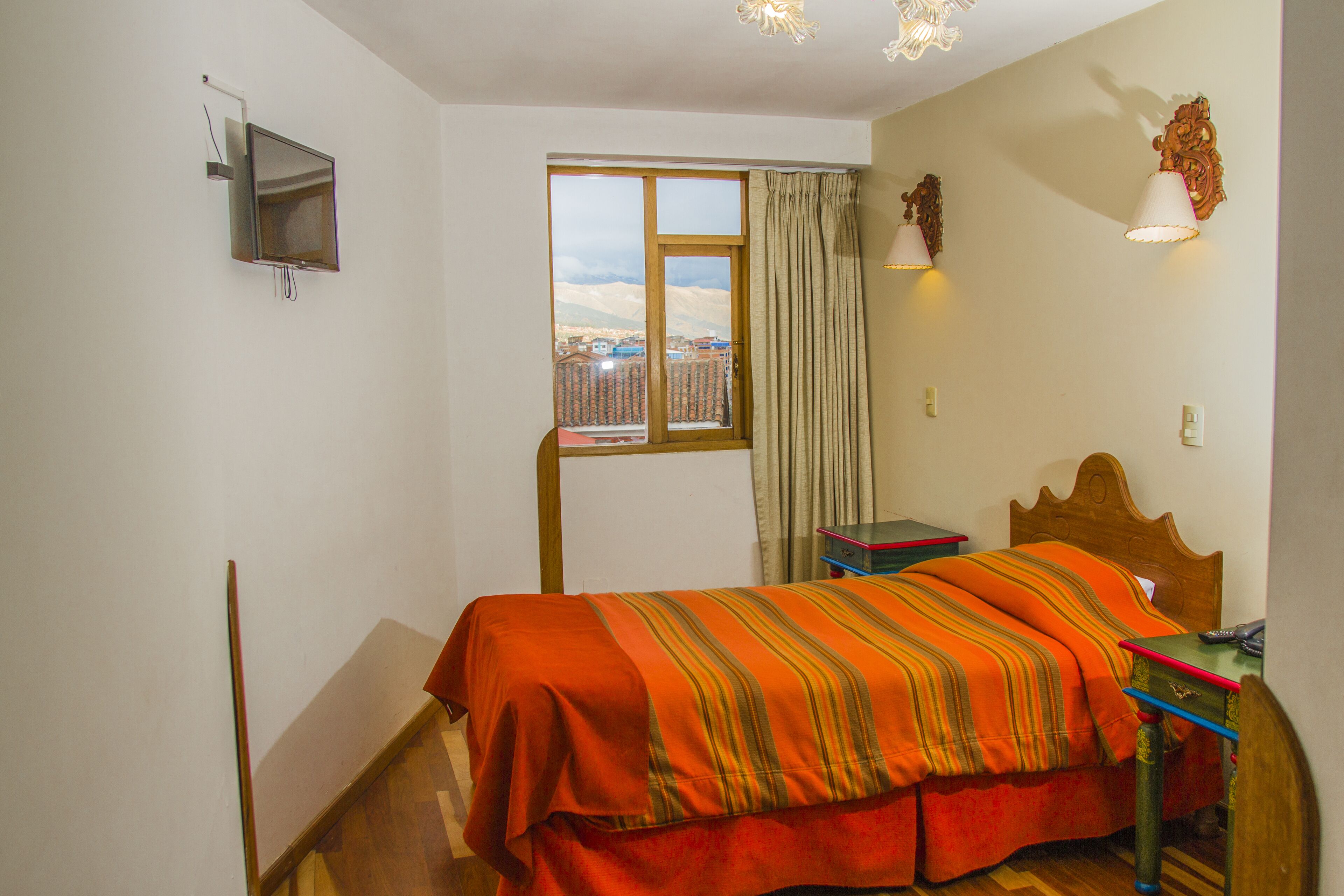 A bedroom with a bed, a desk, a chair, a window with curtains, and a mounted television.