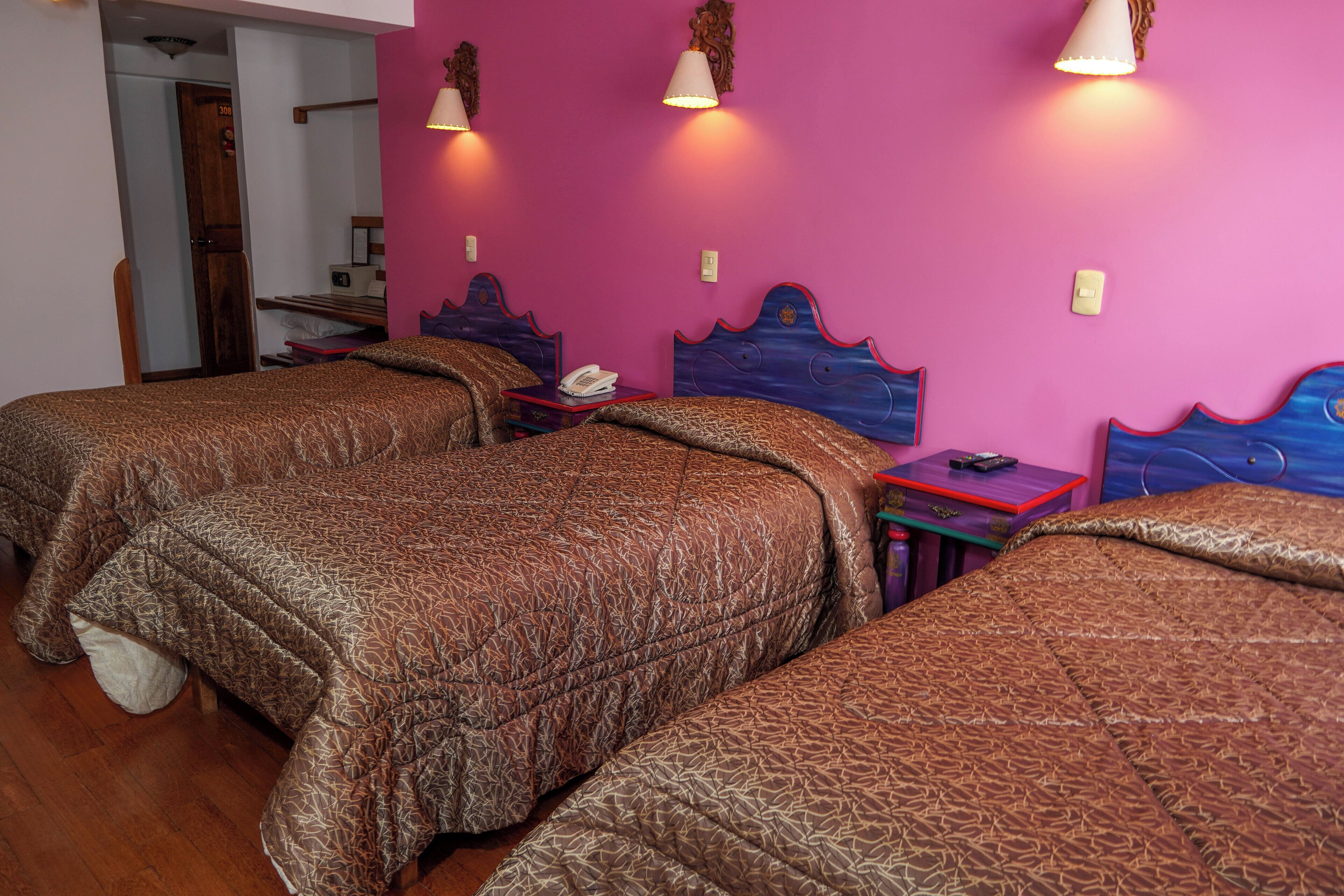A hotel room with two beds, wooden headboards, a small table with a telephone, and a door leading to another room.