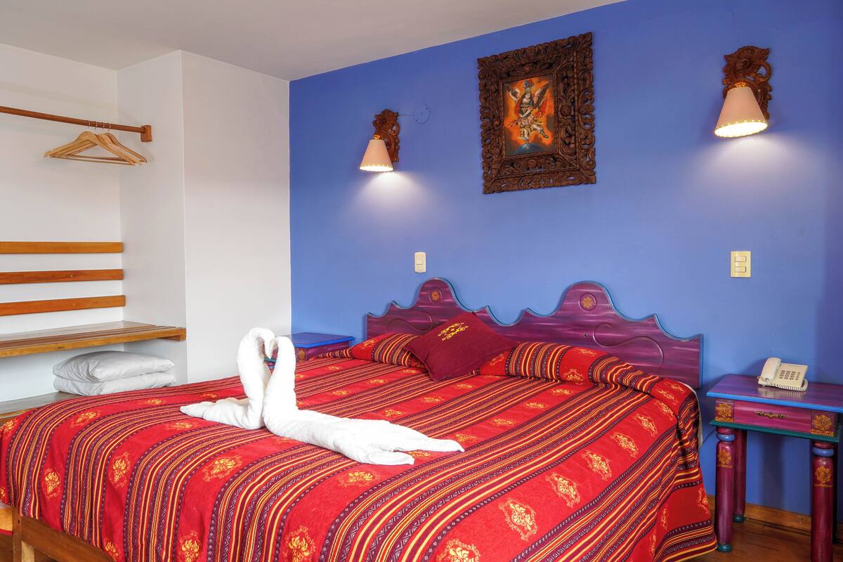 Un dormitorio con cama, armario de madera, mesita de noche con teléfono y una lámpara de pared.