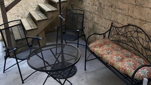 Eine Terrassenfläche mit einem runden Metalltisch, zwei Stühlen, einer Bank mit gemustertem Kissen und einem roten Sonnenschirm.