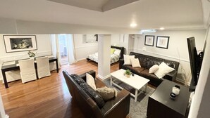 Ein modernes Wohnzimmer mit Sofa, Couchtisch und Fernseher. Es gibt einen Essbereich mit Tisch und Stühlen. Das Zimmer verfügt über ein großes Fenster und eine Tür zu einem anderen Raum.