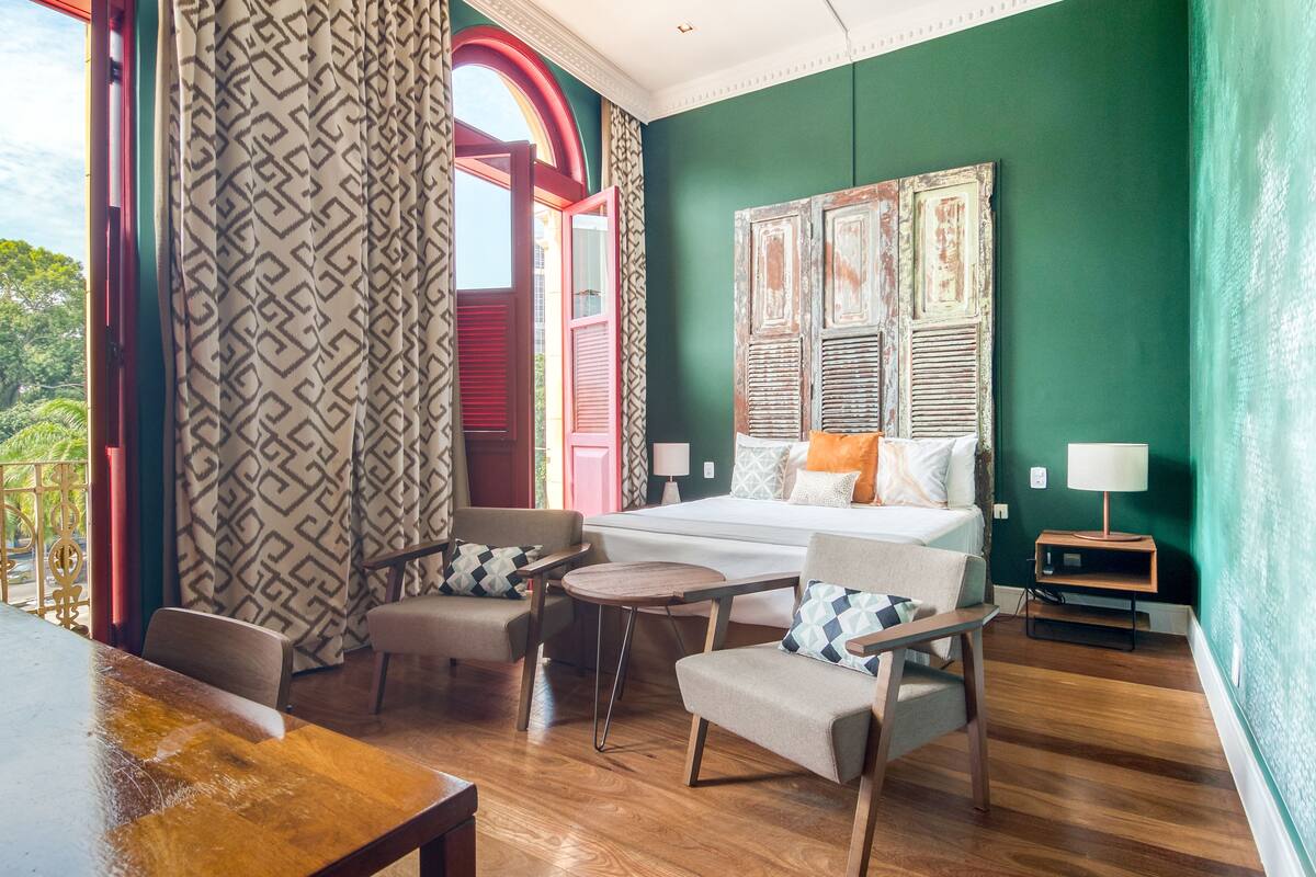 A room with a bed, two armchairs, a small table, and a wooden floor.