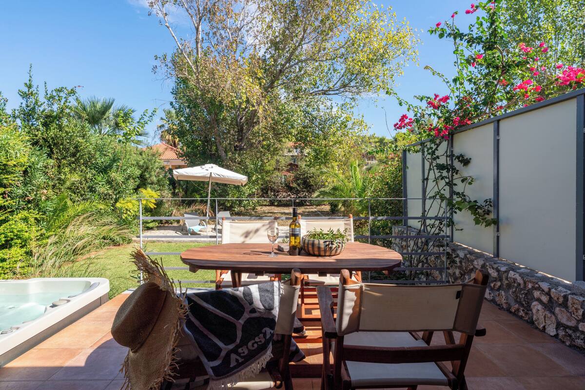 An outdoor patio with a wooden table, chairs, a hot tub, and a stone wall.