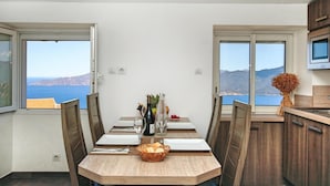 A dining area with a view of the sea, a wooden table, chairs, a basket of bread, and a bottle of wine. - Résidence de la Tour (Piana)