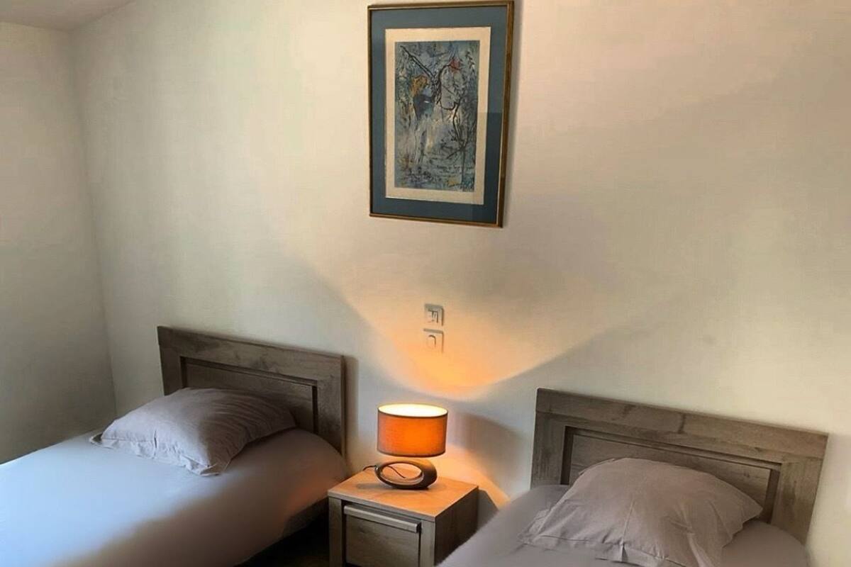 A room with two single beds, a nightstand with a lamp, and a framed picture on the wall.
