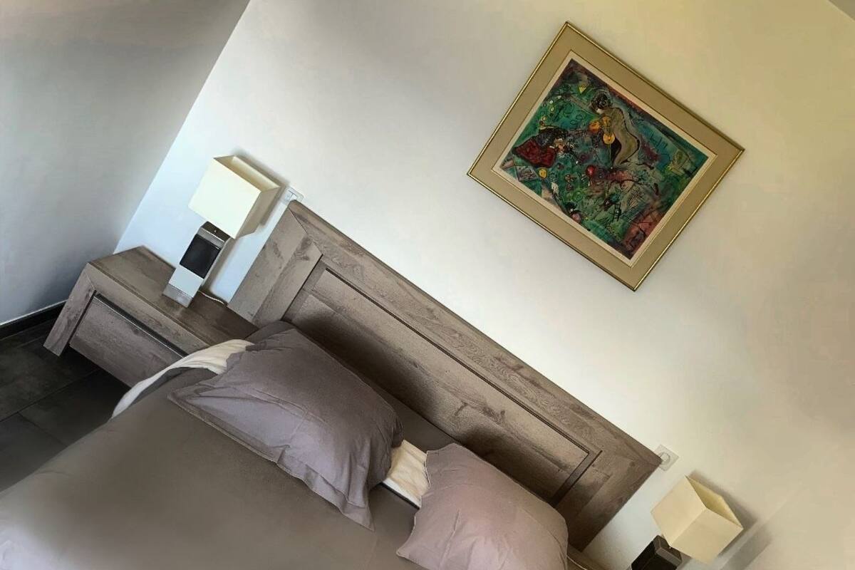 A neatly made bed with a wooden headboard, two bedside tables with lamps, and a colorful painting on the wall.