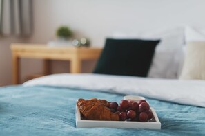 A bed with a blue blanket, a white tray with a croissant and grapes, and a bedside table with a lamp. - P&O Apartments Namysłowska (Warsaw)