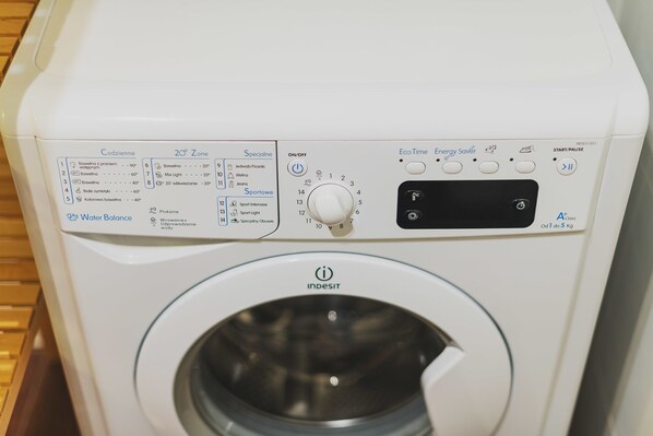 A front view of a white washing machine with a control panel, including a dial and various buttons. - P&O Apartments Namysłowska (Warsaw)