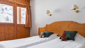 A bedroom with two beds, wooden headboards, and a window with curtains.