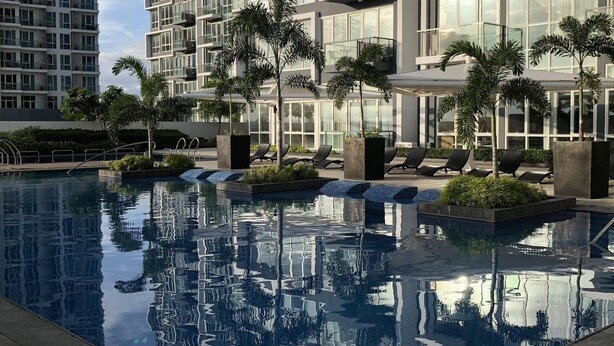A modern residential building with a swimming pool, surrounded by palm trees and concrete planters. - Room with a sea and city view!!  (Lapu Lapu)