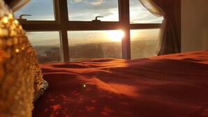 A room with a large window, a bed with a red blanket, and a view of the cityscape during sunset. - Room with a sea and city view!!  (Lapu Lapu)
