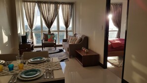 A living room with a sofa, a chair, a dining table set with plates and cutlery, and a view of the city through large windows. - Room with a sea and city view!!  (Lapu Lapu)