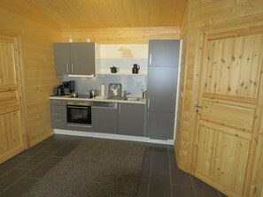 A compact kitchen with grey cabinets, a stainless steel refrigerator, and a wooden ceiling.