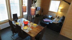 A cozy cabin interior with a dining table set for four, a sofa, and a small TV.