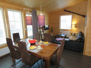 A wooden interior with a dining table set for two, a sofa, and a television in a living area.