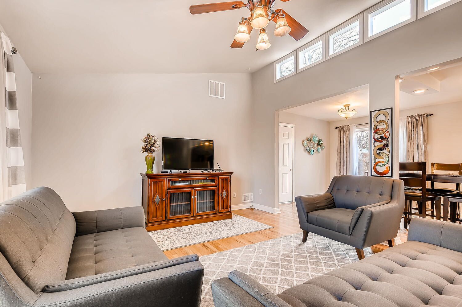 A spacious living room with a large grey sofa, a smaller grey armchair, and a wooden entertainment unit with a flat-screen TV.