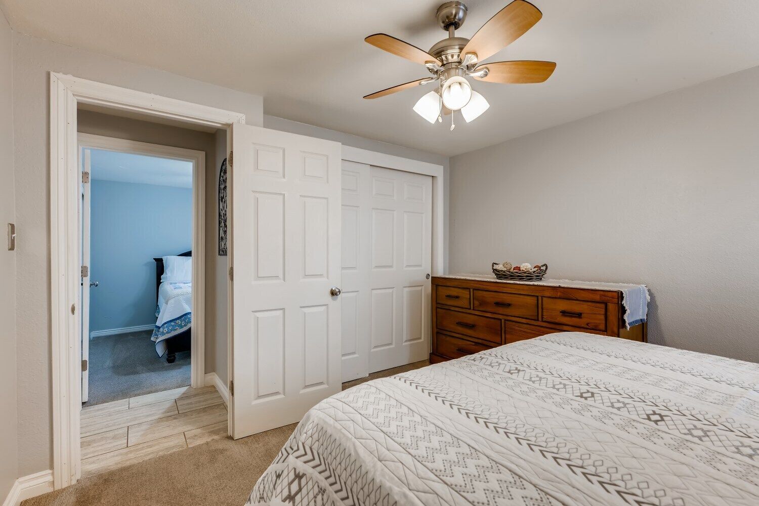 Un dormitorio con cama, cómoda, ventilador de techo y puerta que da a otra habitación.