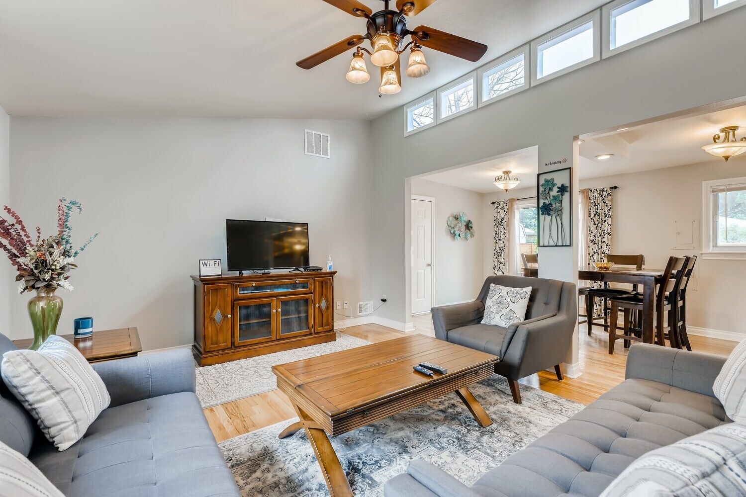 A spacious living room with a large flat-screen TV, a wooden coffee table, and grey sofas.