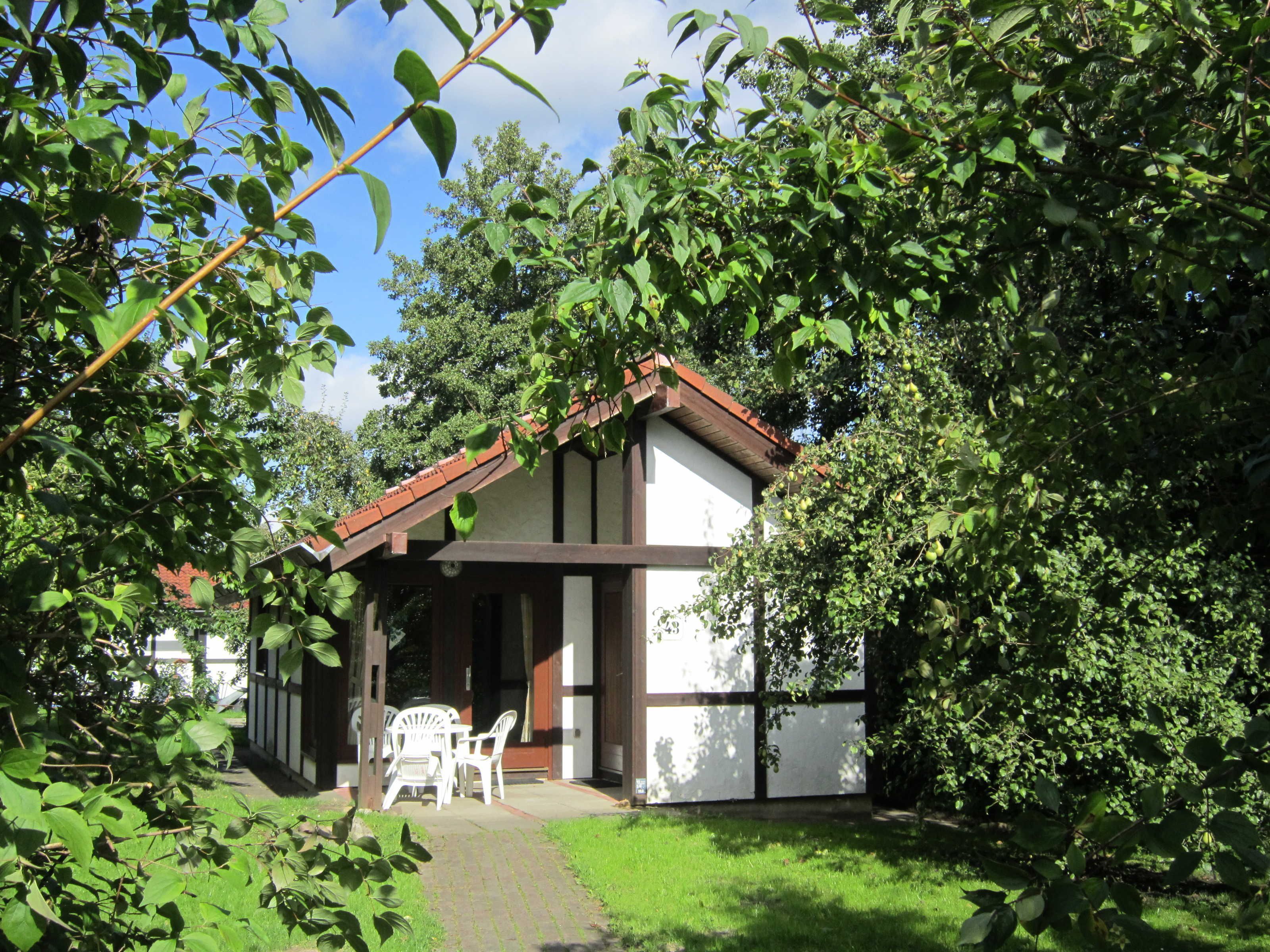 A small house with a tiled roof, surrounded by lush greenery and trees.