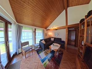 A cozy living room with a wooden ceiling, a sectional sofa, a coffee table, and a bookshelf.