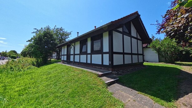 Ett traditionellt hus med korsvirkesfasad, ett sluttande tak, en veranda och en välskött gräsmatta.
