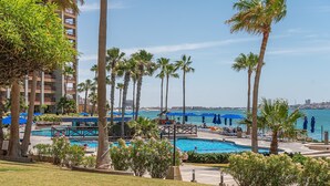 A resort with a pool area, palm trees, and a view of the sea. - Sonoran Sun W-102 Sunset Strip Ground Floor Oceanfront Condo (Puerto Peñasco)
