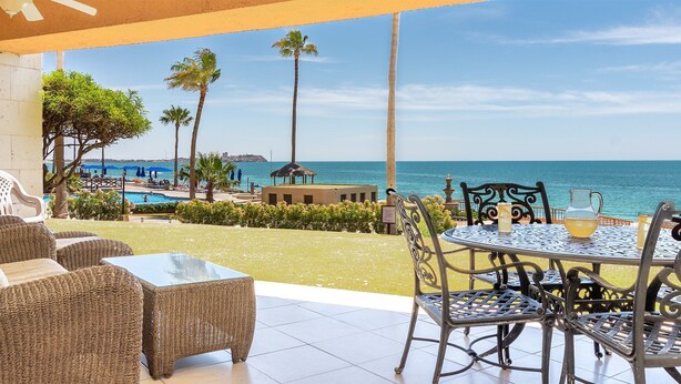 A patio with wicker furniture overlooking a pool and the sea. - Sonoran Sun W-102 Sunset Strip Ground Floor Oceanfront Condo (Puerto Peñasco)