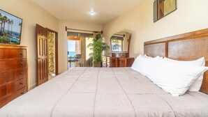 A bedroom with a large bed, wooden dresser, and a view of the outdoors. - Sonoran Sun W-102 Sunset Strip Ground Floor Oceanfront Condo (Puerto Peñasco)