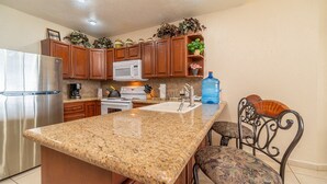 A kitchen with granite countertops, stainless steel appliances, wooden cabinets, and a large water dispenser. - Sonoran Sun W-102 Sunset Strip Ground Floor Oceanfront Condo (Puerto Peñasco)