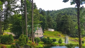 A serene landscape with a stone house, a pond, and a wooden chair.