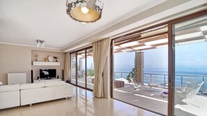 A spacious living room with a white sofa, a flat-screen TV, and a large sliding glass door leading to a balcony with outdoor furniture. - Edem (Corfu)
