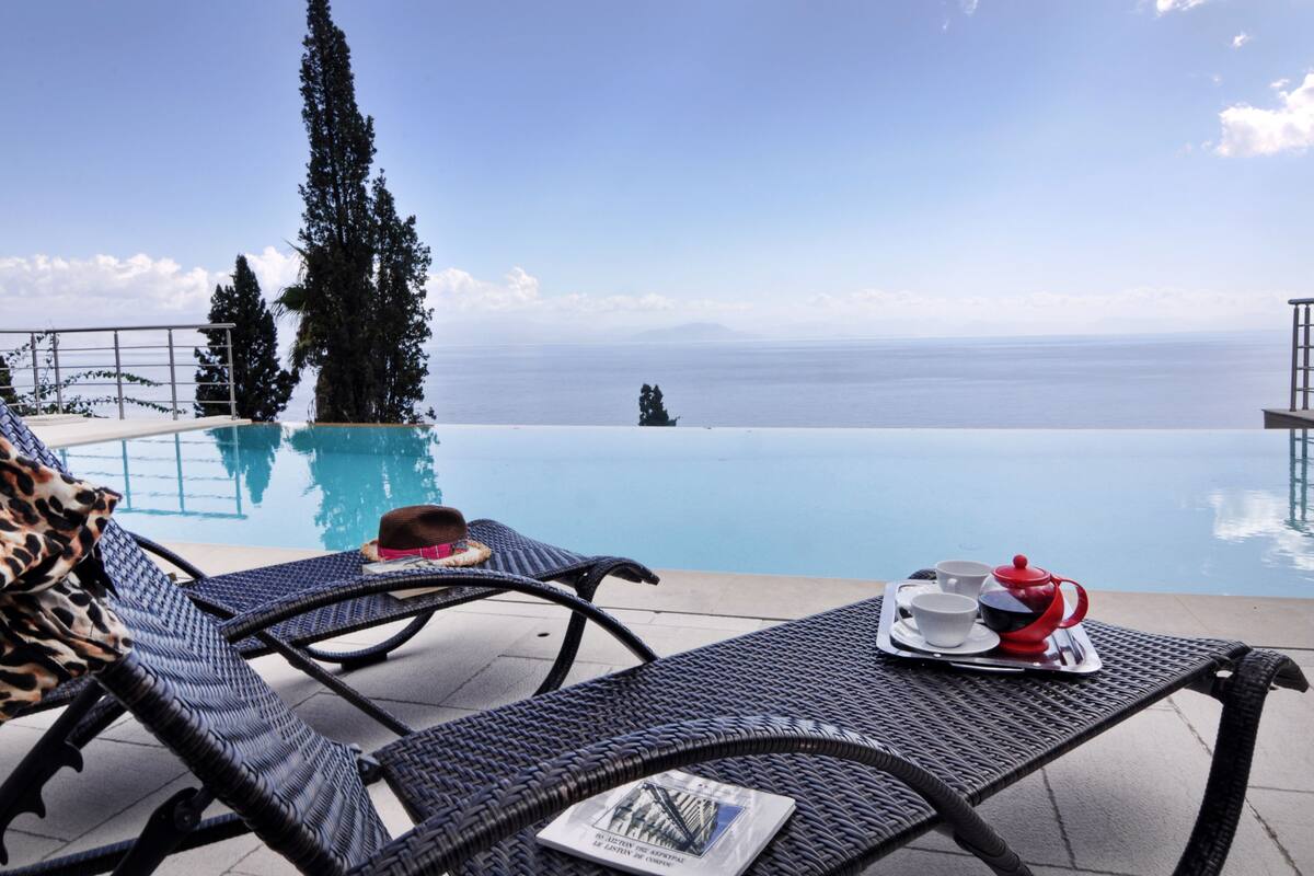 A poolside area with lounge chairs, a table with a tray of tea and cups, and a view of the sea.