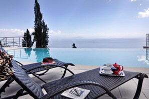 A poolside view with lounge chairs, a table with a teapot and cups, and a view of the sea. - Edem (Corfu)