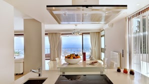A modern kitchen with a central island, a view of the sea, and a dining area with a table and chairs. - Edem (Corfu)