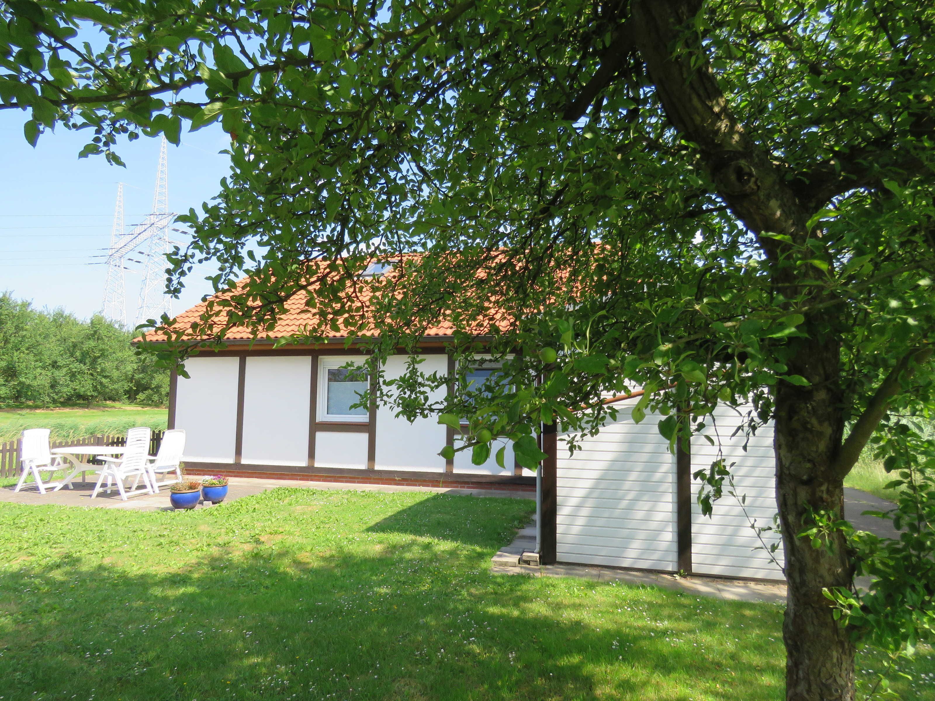 Une petite maison avec un toit en tuiles, une cour clôturée et un arbre au premier plan.