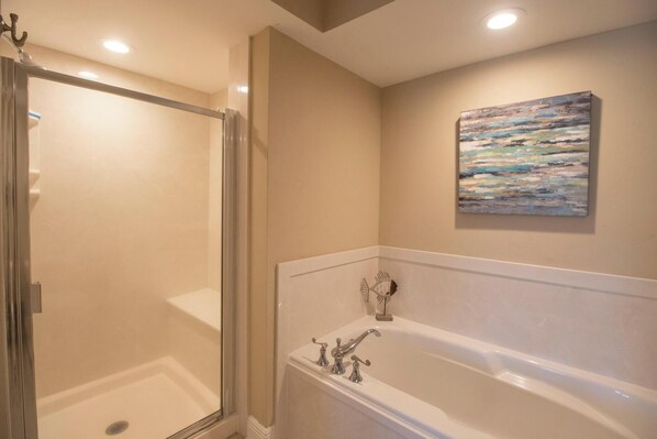 Un baño con cabina de ducha de vidrio, bañera con una escultura decorativa de pez y un cuadro de pared con textura.