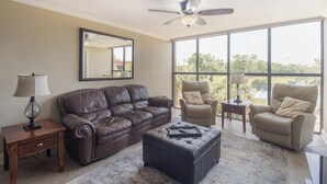 Un salón amplio con un sofá de cuero marrón, dos sillones beige, una mesa de centro y un ventilador de techo.