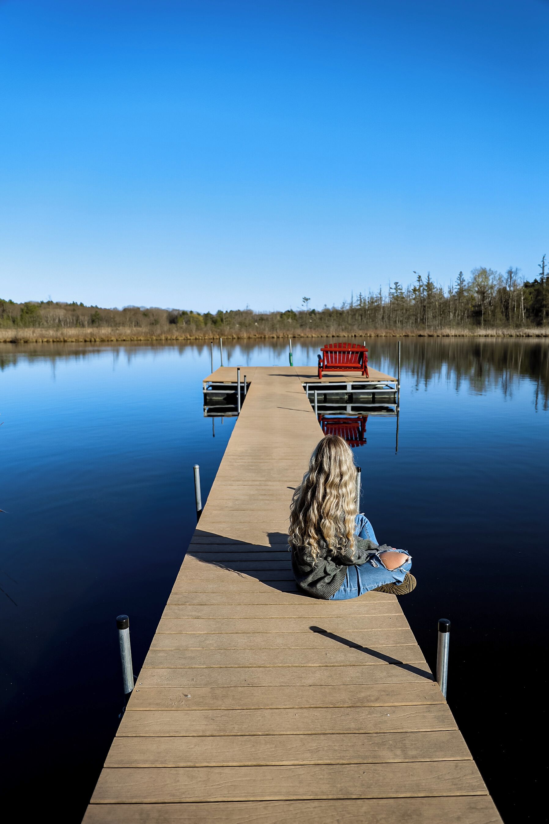 Une jetée en bois s’étendant sur une étendue d’eau calme, avec un banc rouge à son extrémité.