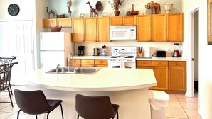 A kitchen with wooden cabinets, a white refrigerator, a microwave, a stove, and a sink. There are two chairs at the island.