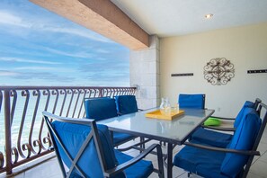 A balcony with a glass table, blue chairs, and a decorative wall piece. - Sonoran Sun W-806 Chasing The Sun Great Oceanfront Condo (Puerto Peñasco)