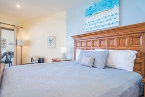 A hotel room with a large bed, a wooden headboard, a painting on the wall, and a chair by the window.