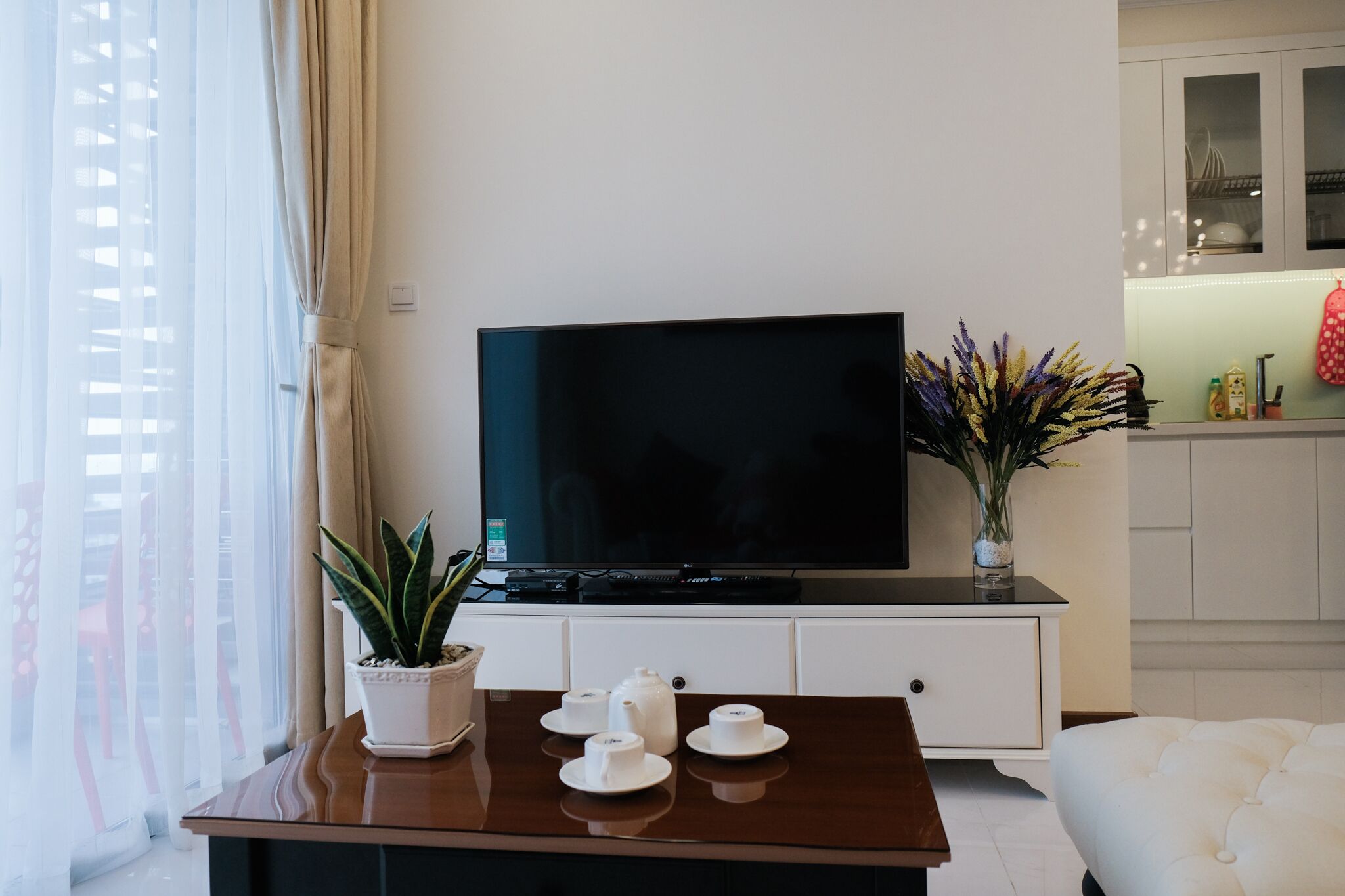 A modern living room with a flat-screen TV on a wooden table, a potted plant, and a vase of flowers.