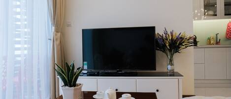 A modern living room with a flat-screen TV on a wooden table, a potted plant, and a vase of flowers.