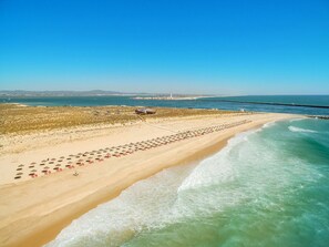 Una playa con filas de tumbonas y sombrillas, cielo despejado y un faro a lo lejos.