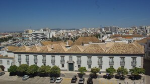 Un edificio blanco con techo de tejas, rodeado de coches aparcados y árboles.